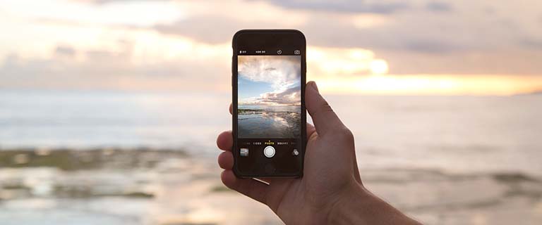 Hand holding phone, capturing ocean sunset.