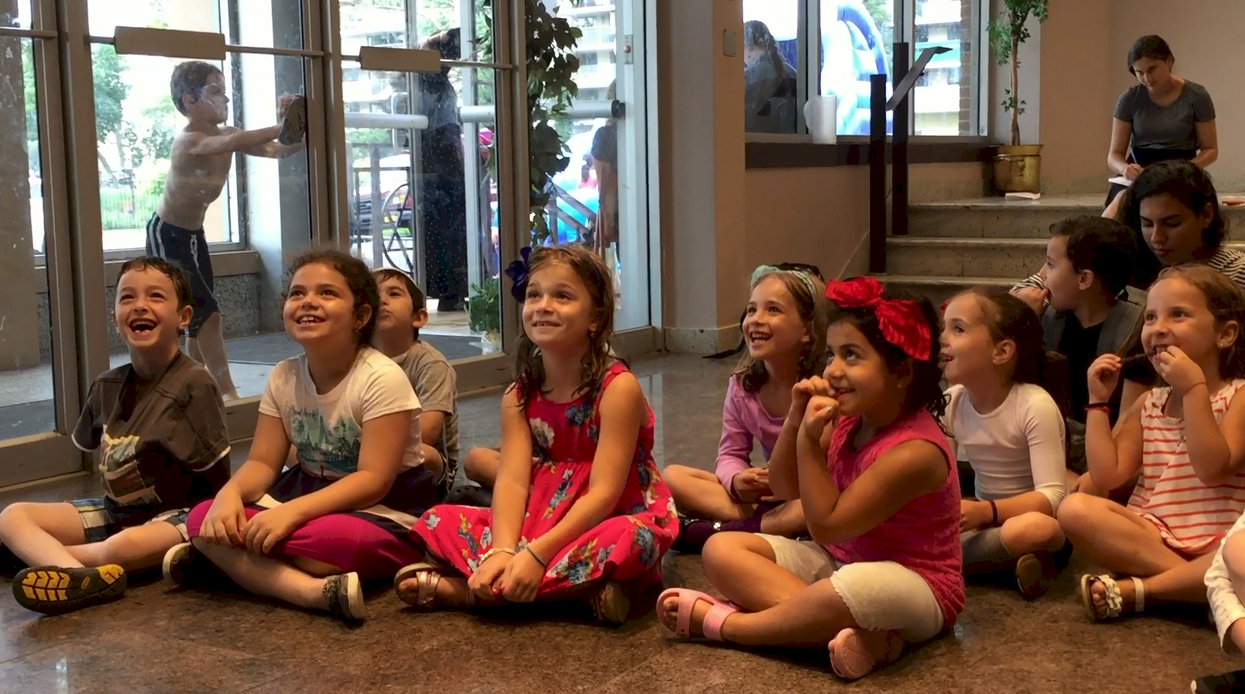 Children sitting indoors, smiling and attentive.