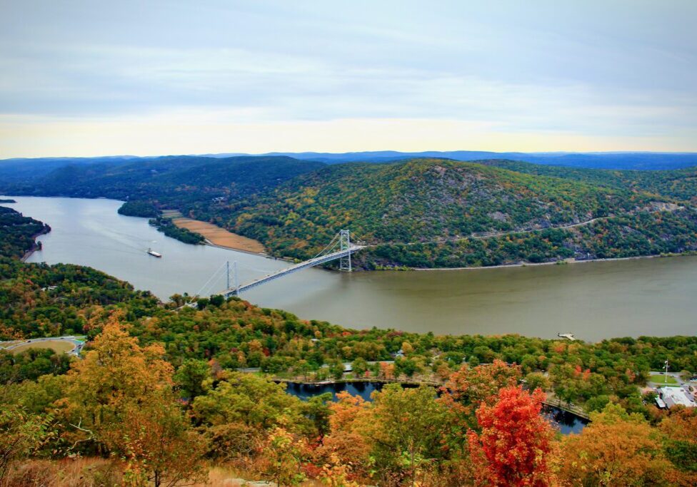 Bear Mountain Bridge in Autumn is a photograph taken just before dusk on a warm and overcast day in early Autumn looking East over the Hudson River and Bear Mountain as a barge is being towed.