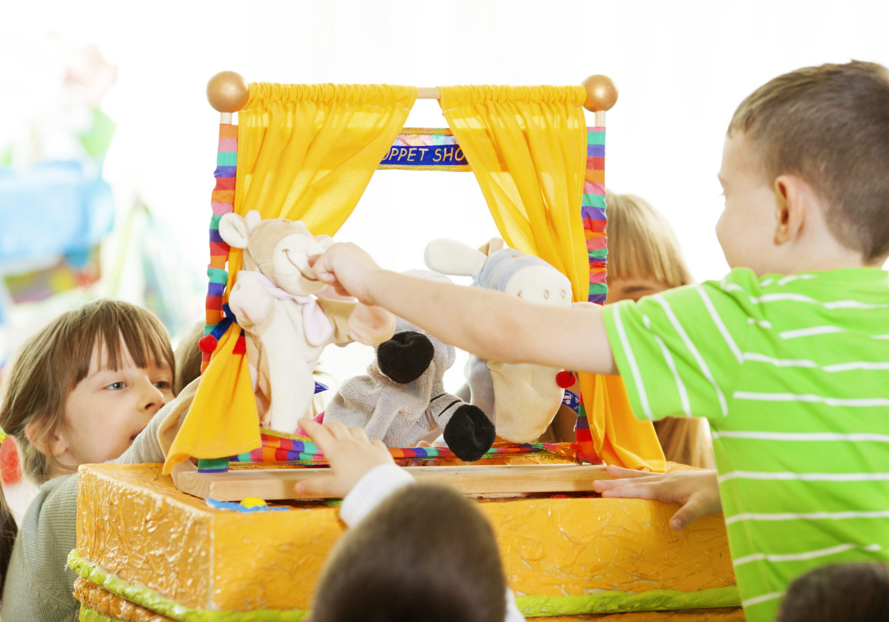 Group of preschool children having craft activities at preschool, playing puppet show. Finger puppets, two children and teacher are audience. Selective focus to little girl making puppet show.
